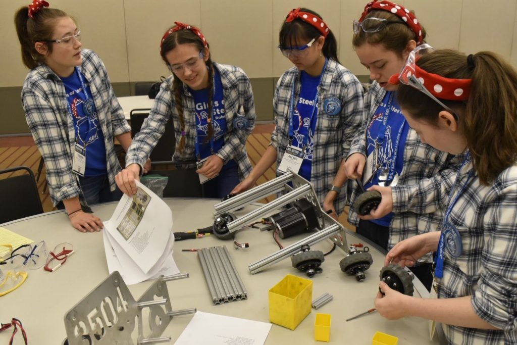 A photo of a group of five teens building a robot car together.