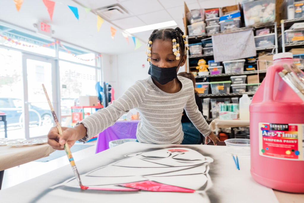 A child leans over a table to paint in the colors of a spray-painted design at the Afro Futurism event.