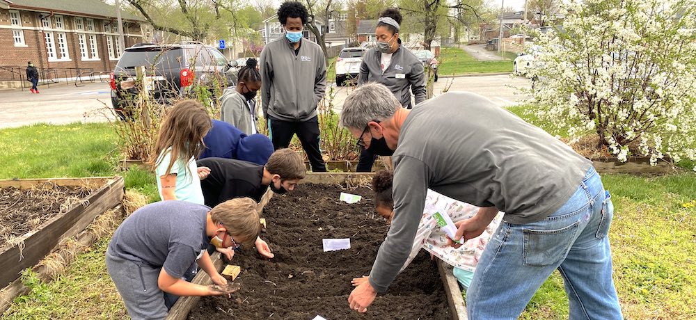 Nine people lean over and are digging into an upraised bed of dirt.