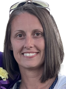 A smiling woman with shoulder-length straight brown hair with glasses pushed up on top of her head