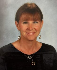 A smiling woman with straight red hair and bangs wearing a black shirt