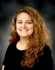 Woman with curly long brown hair wearing a black shirt