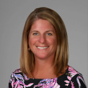Woman with long straight brown hair to shoulders wearing a pattern shirt